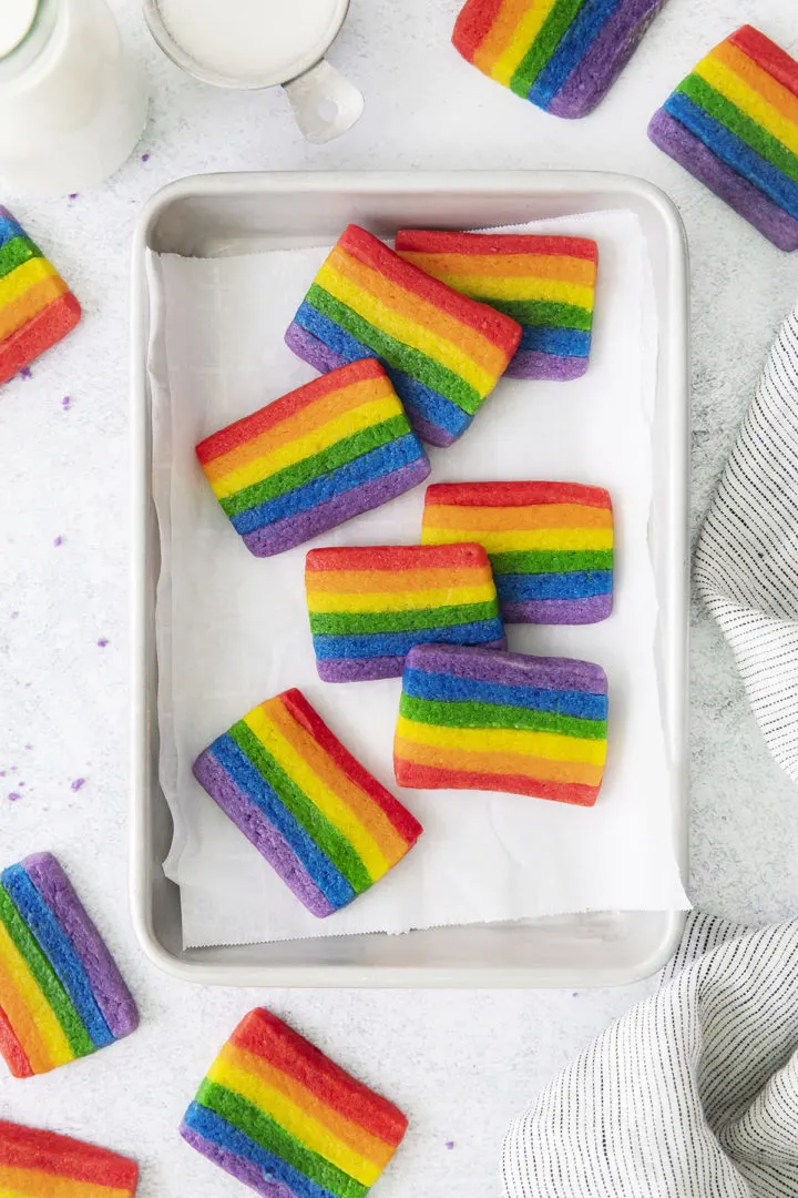 photo of a baking sheet with rainbow cookies for st patrick's day on it next to a cup of milk