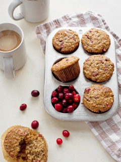 photo of cranberry muffins in a muffin tin next to fresh cranberries and coffee mugs