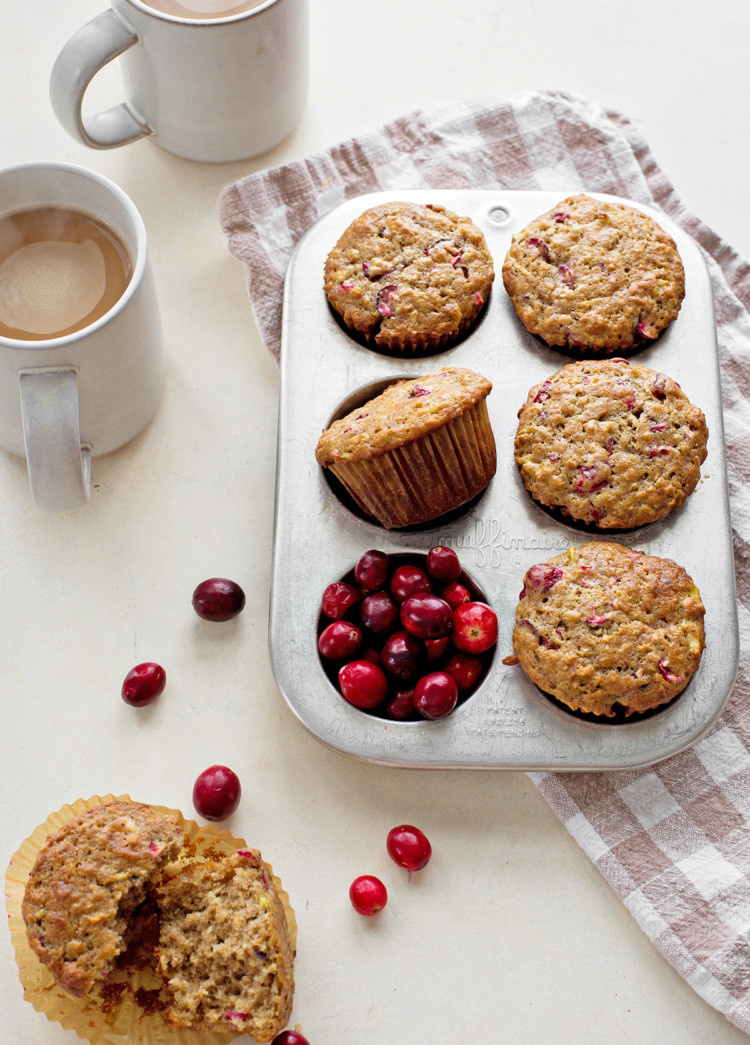 photo of cranberry muffins in a muffin tin next to fresh cranberries and coffee mugs