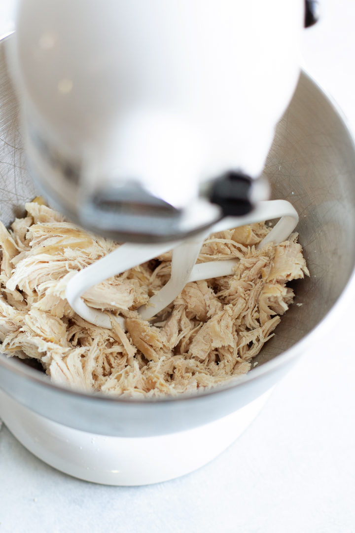 cooked chicken being shredded in a stand mixer