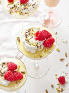 white chocolate pudding in a variety of glass dishes, garnished with whipped cream and raspberries, on a white background