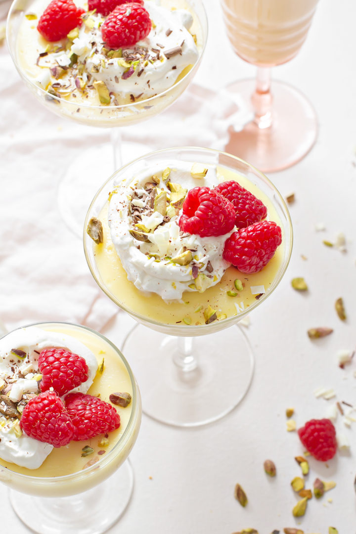 photo of white chocolate pudding with whipped cream, raspberries, pistachios, and shaved chocolate for an easy valentine's day dessert recipe