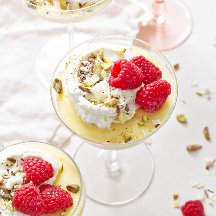 white chocolate pudding in a variety of glass dishes, garnished with whipped cream and raspberries, on a white background