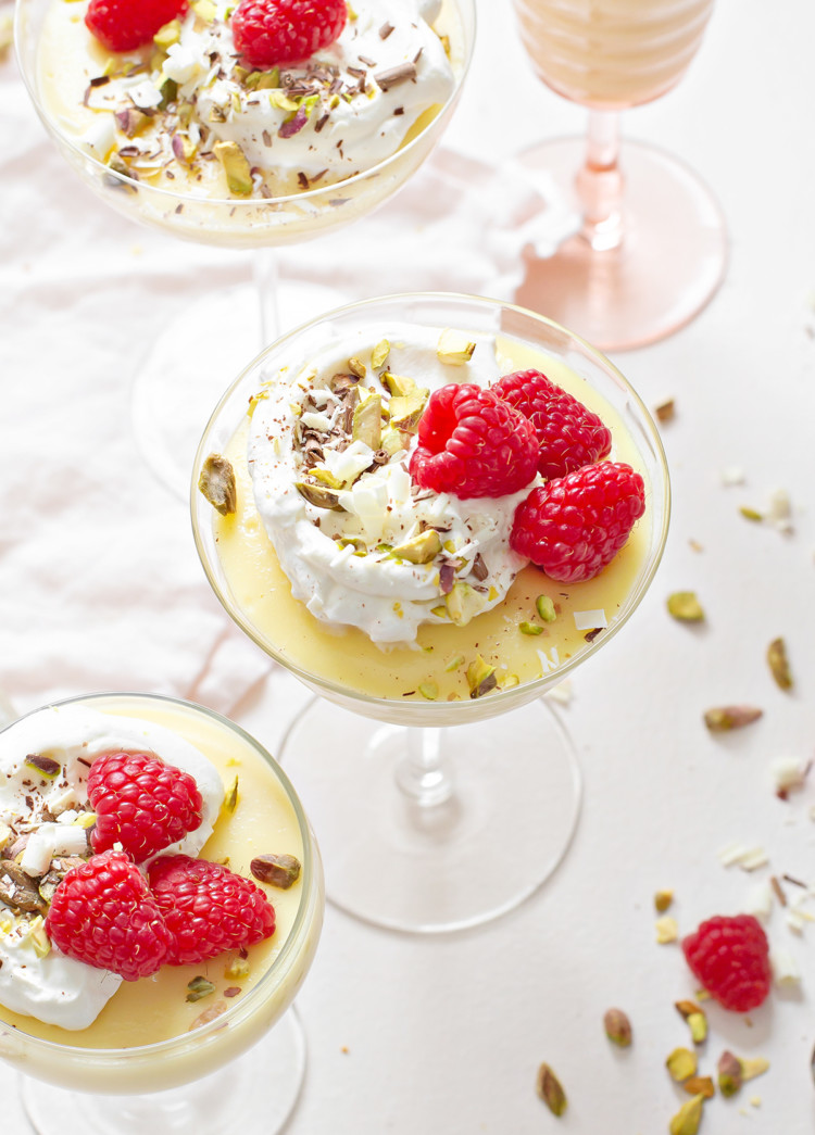 white chocolate pudding in a variety of glass dishes, garnished with whipped cream and raspberries, on a white background