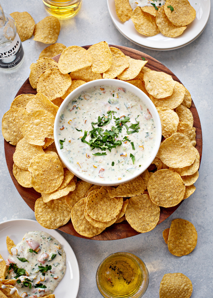 overhead photo of queso blanco in a white bowl with chips and beer