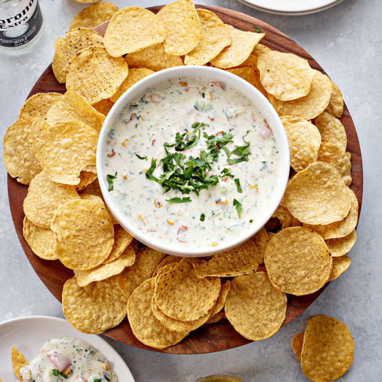 overhead photo of queso blanco in a white bowl with chips and beer