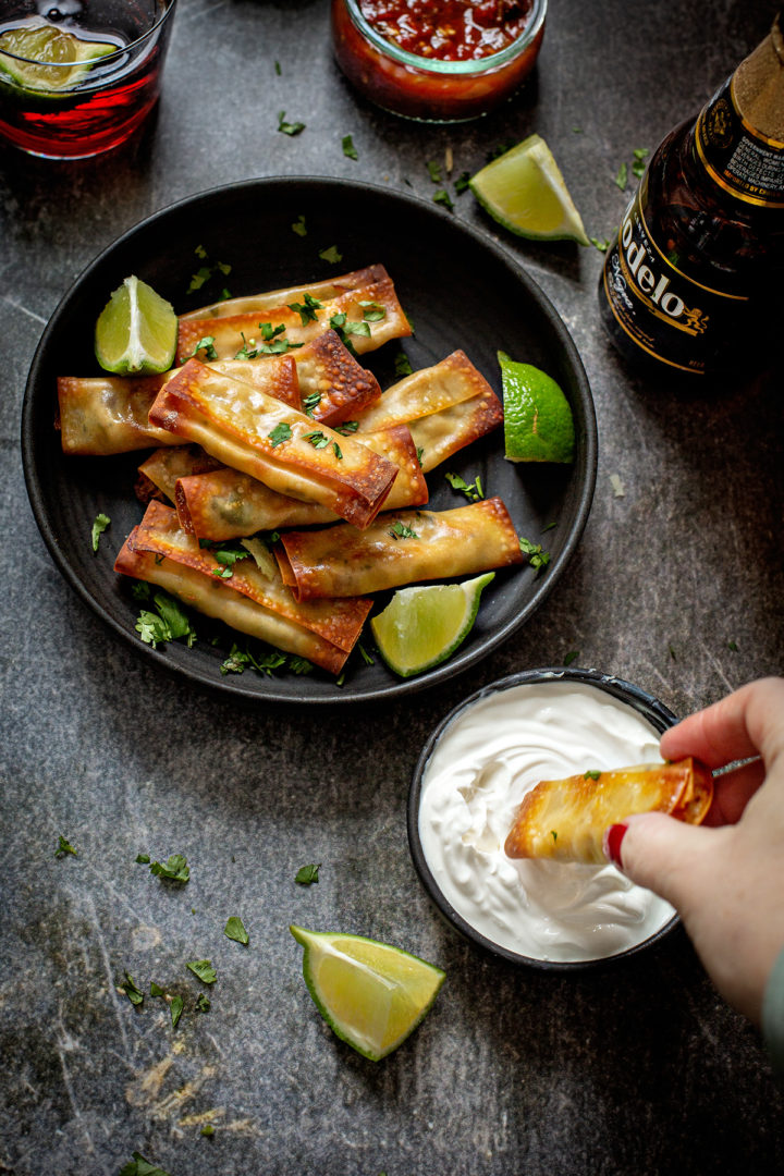 woman dipping a chicken taquito into a bowl of sour cream