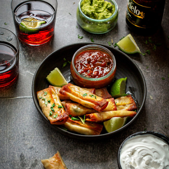 chicken taquitos on a black serving dish with bowls of salsa and guacamole