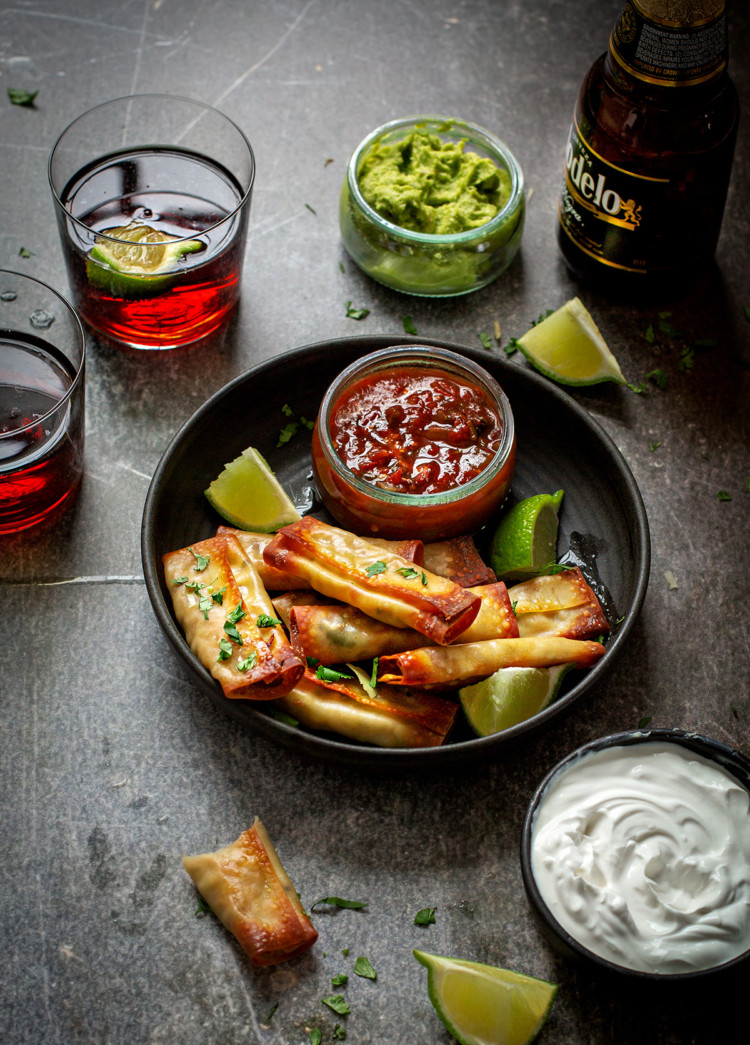 chicken taquitos on a black serving dish with bowls of salsa and guacamole