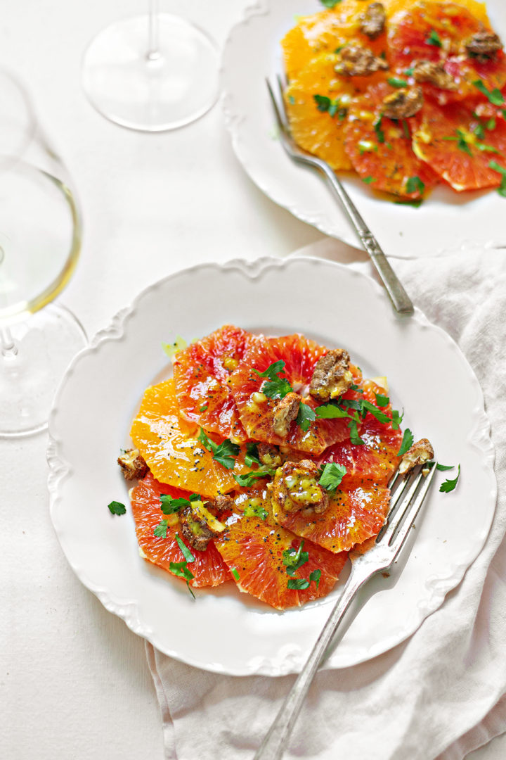 two white dishes on a white table plated with citrus salad