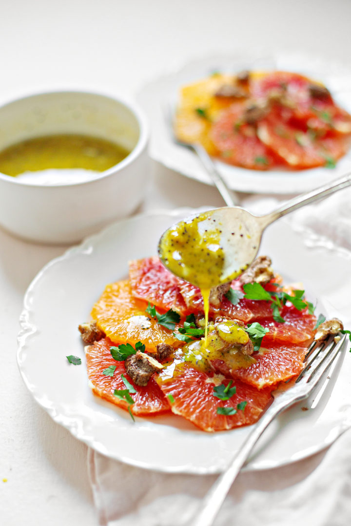 spoon pouring poppy seed dressing onto a plate of citrus salad