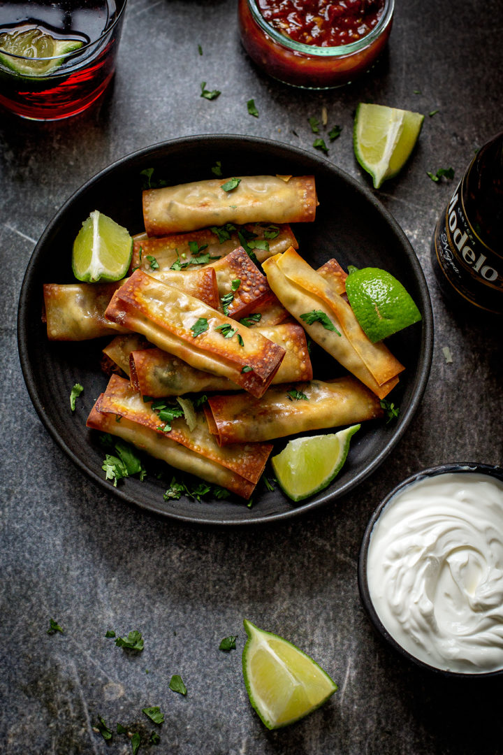 overhead photo of a plate of chicken and cheese taquitos with lime wedges and cilantro