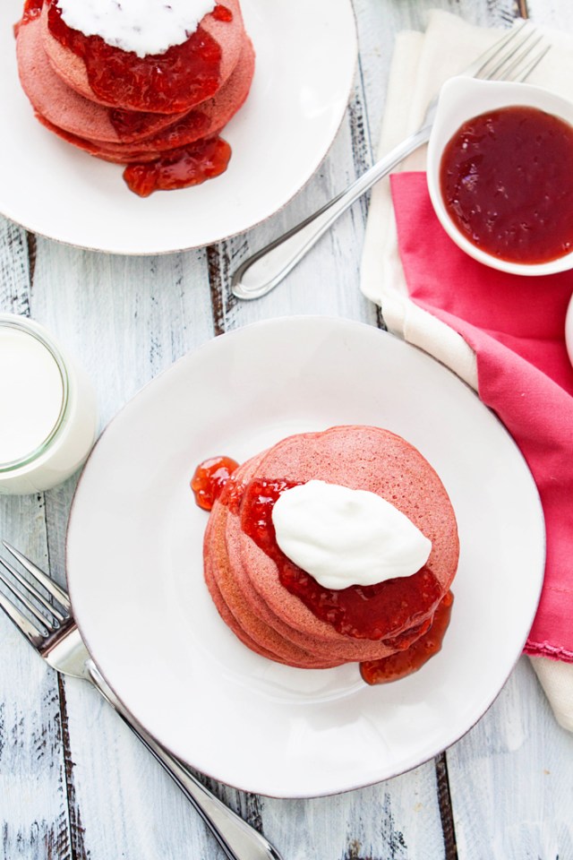 Overhead photo of a white rustic table set with plates of pink beet pancakes for valentine's day