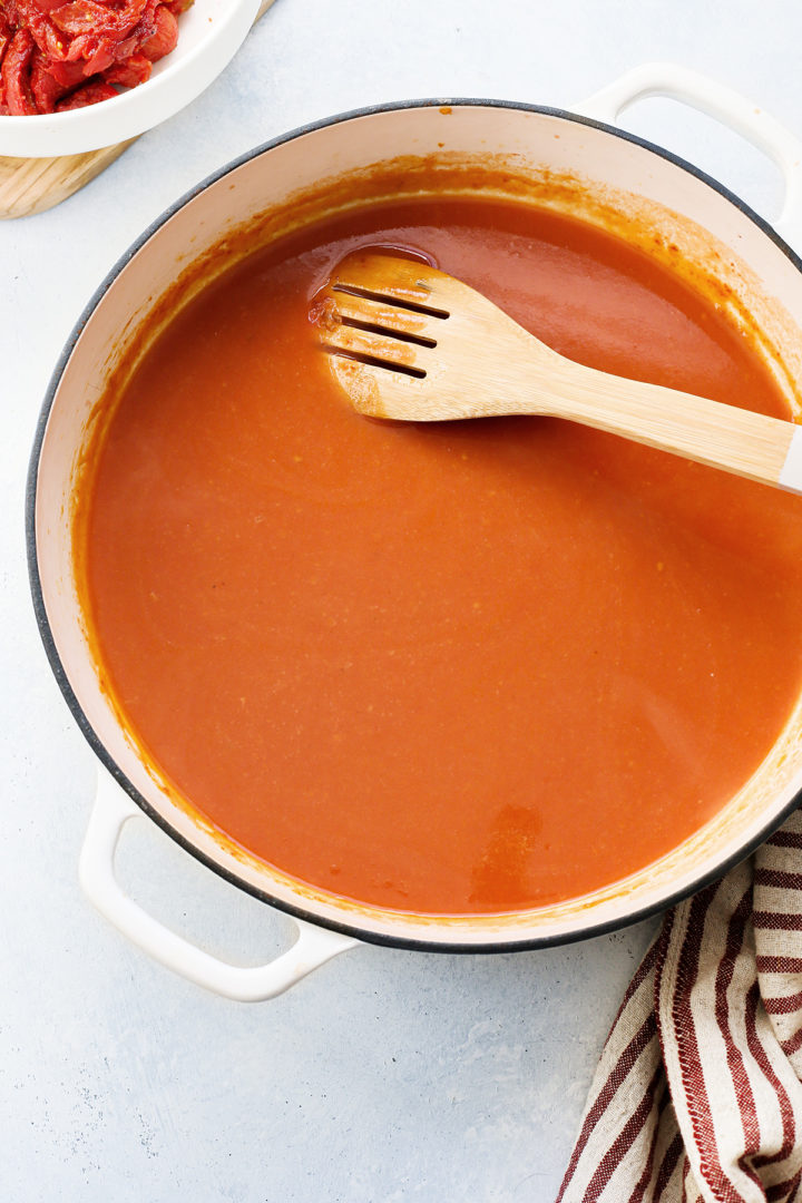 cream of tomato soup cooking in a white cast iron pot being stirred with a wooden spoon