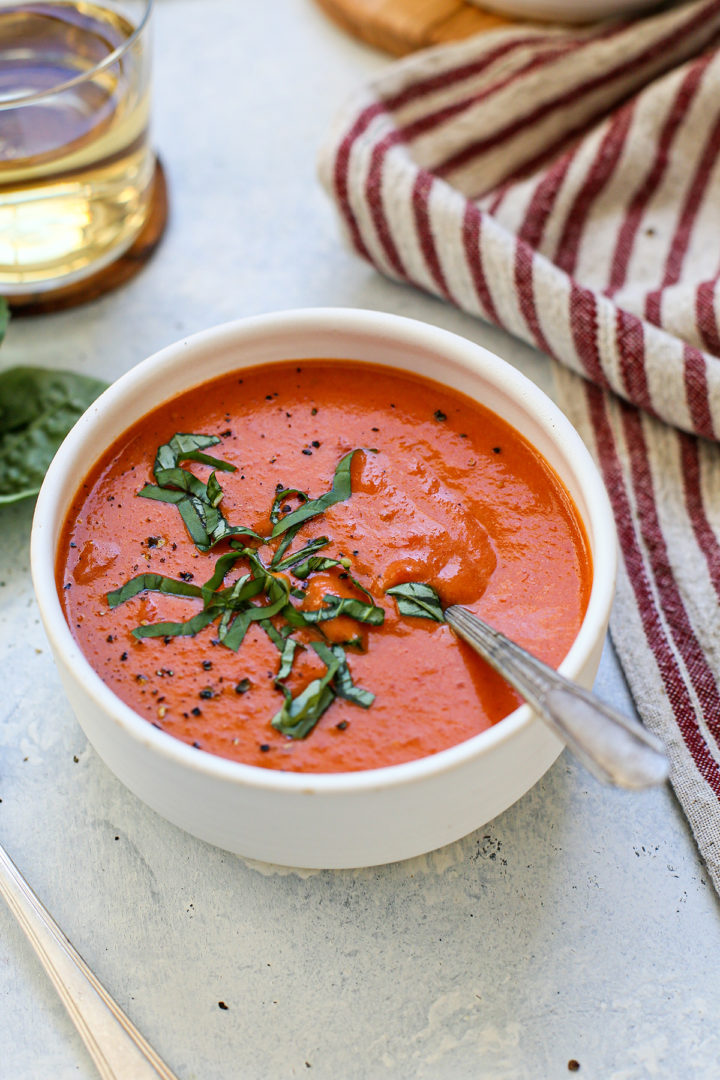 cream of tomato soup being served in a white bowl with a spoon topped with fresh basil