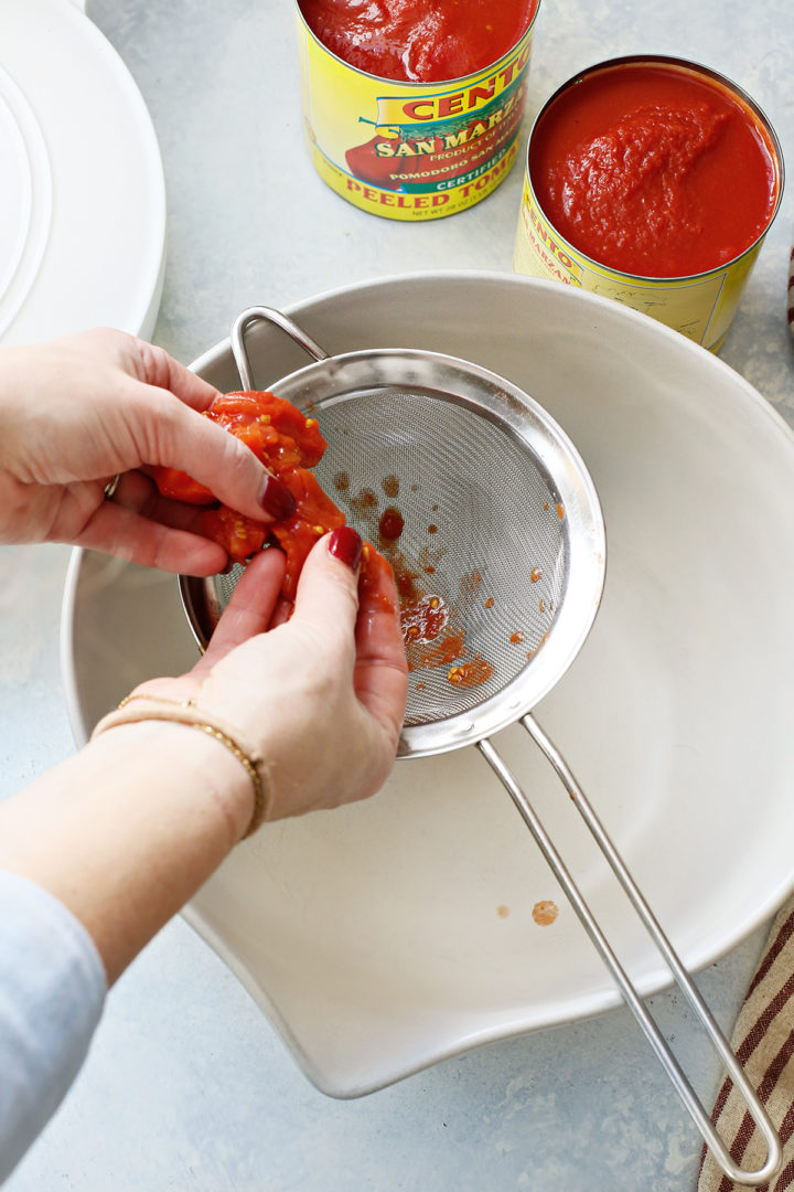 woman deseeding whole tomatoes to make homemade tomato soup