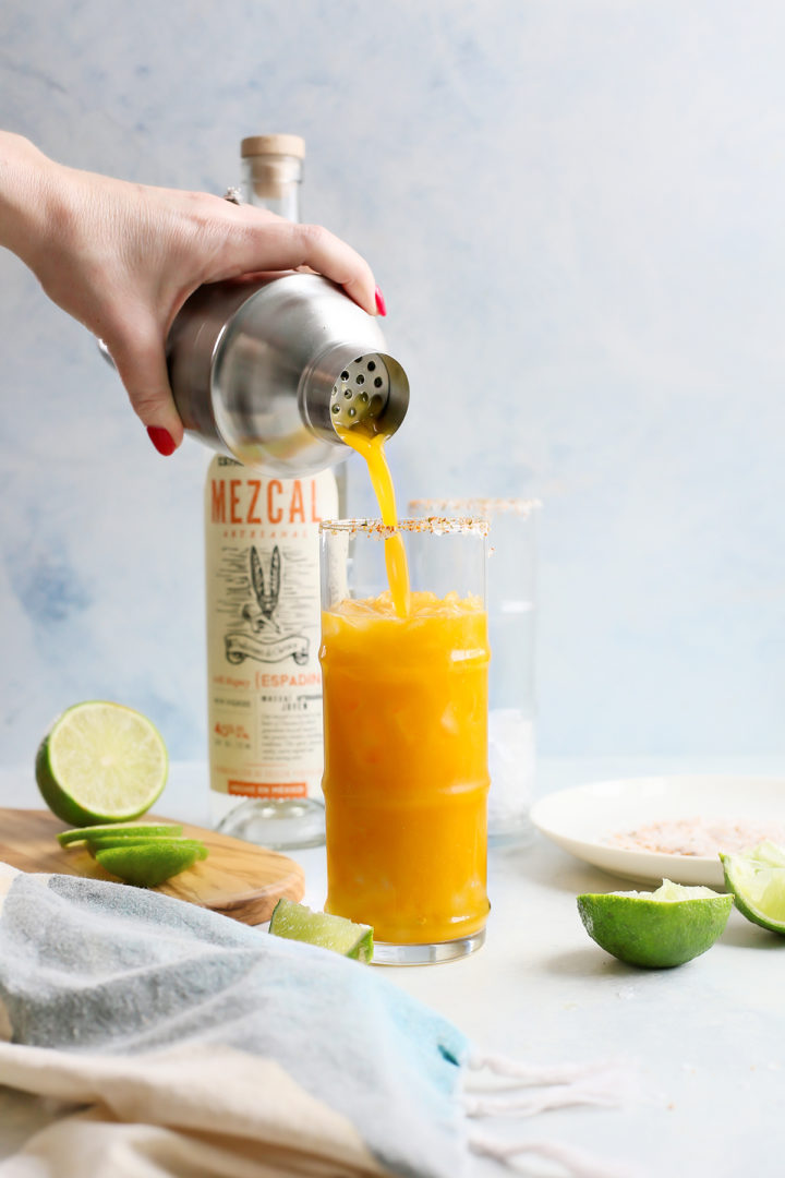 woman pouring this passion fruit cocktail into a glass with ice and spicy salt rim