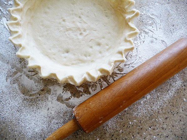 pie plate with homemade quiche crust to make caramelized onion quiche on a kitchen counter next to a rolling pin