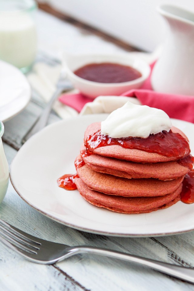 close up photo of a stack of pink velvet pancakes on a white plate