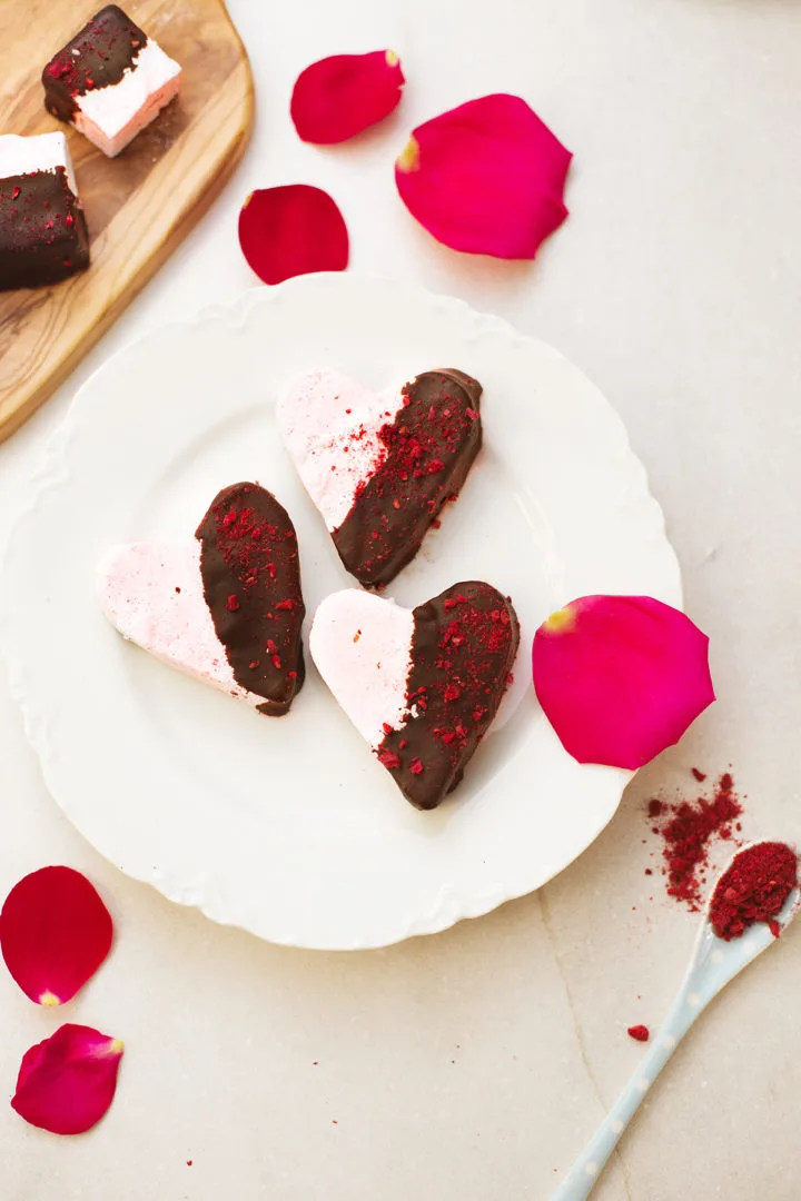 dark chocolate covered raspberry marshmallows on a white plate next to a cutting board