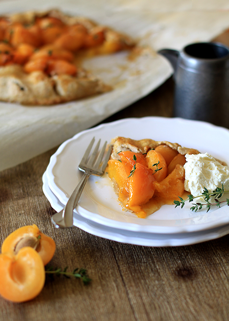 photo of a slice of apricot galette on a white plate with whipped cream and a fork