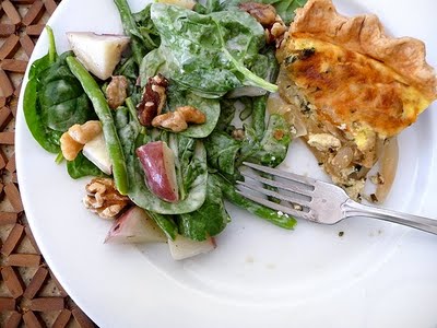 white plate with a salad, a slice of cheese and onion quiche, and a fork