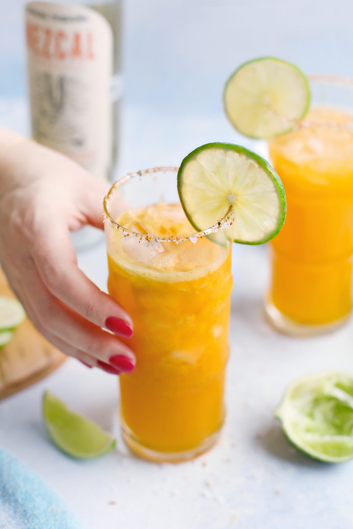 woman picking up a glass of passion fruit margarita