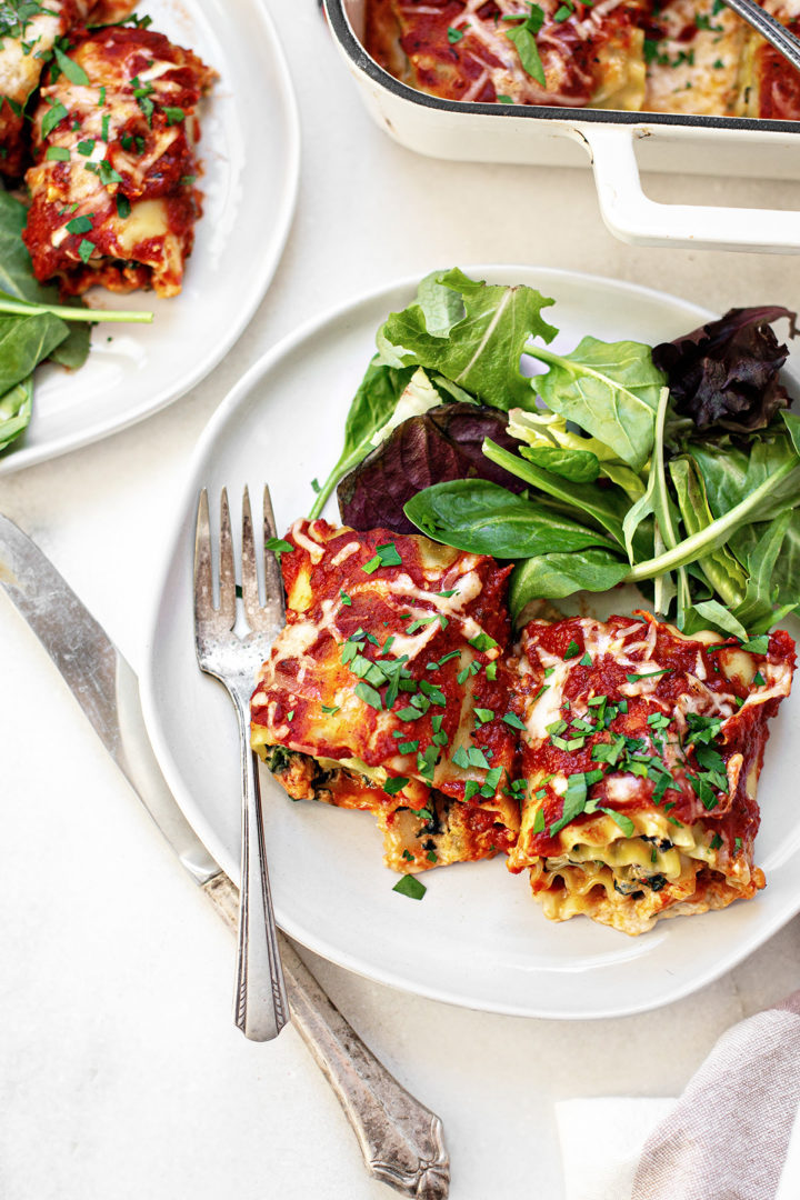 overhead photo of a white plate with two spinach lasagna roll ups on it