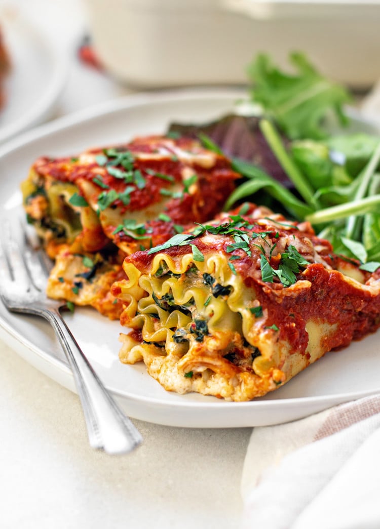 two spinach lasagna rolls on a white plate with a fork and green salad