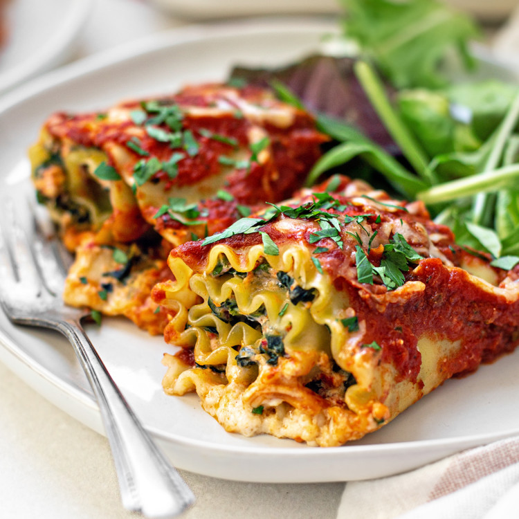 two spinach lasagna rolls on a white plate with a fork and green salad