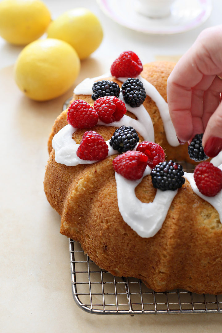 A woman arranges fresh raspberries and blackberries on top of the lemon ricotta bundt cake 