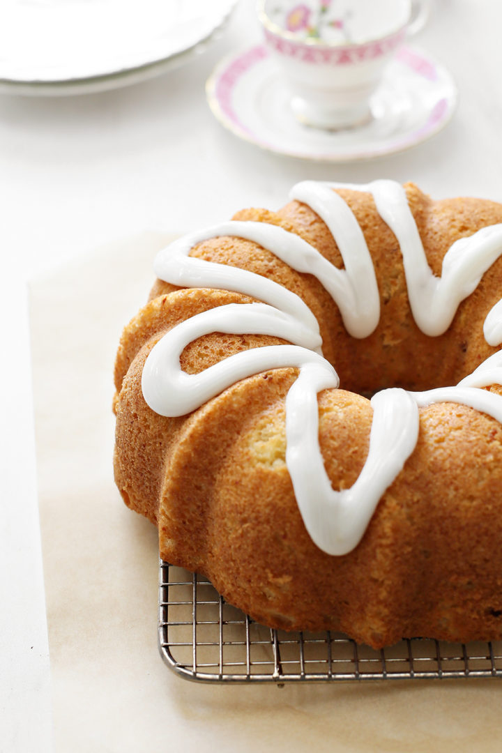 The lemon ricotta bundt cake is now fully coated in lemon glaze, sitting on a wire rack with parchment paper underneath.