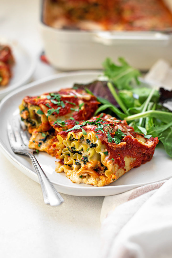 a plate of roll up lasagna with spinach on a white table