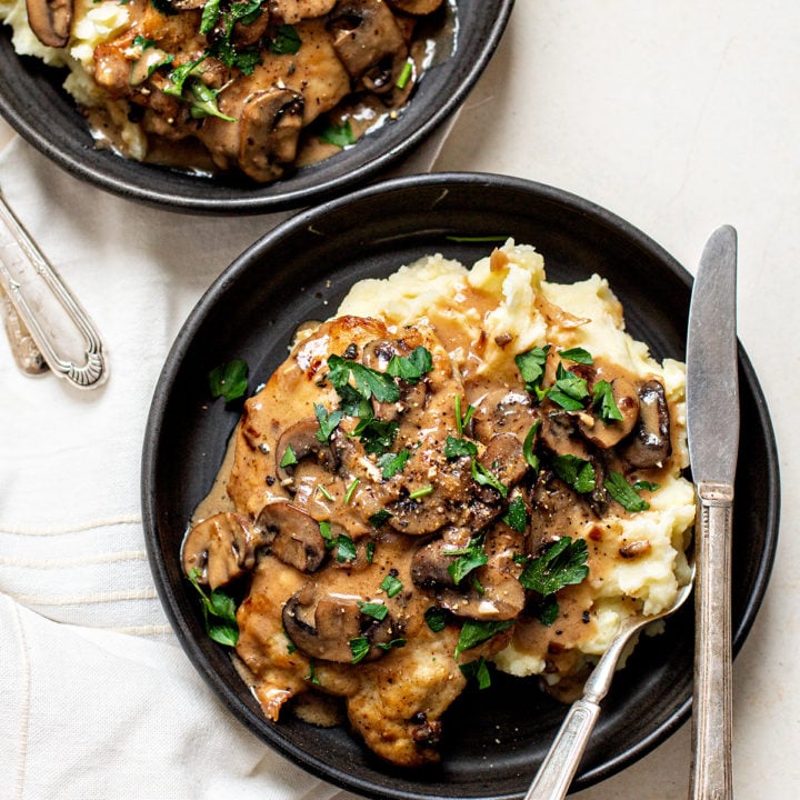 two black dishes plated with chicken marsala and mashed potatoes