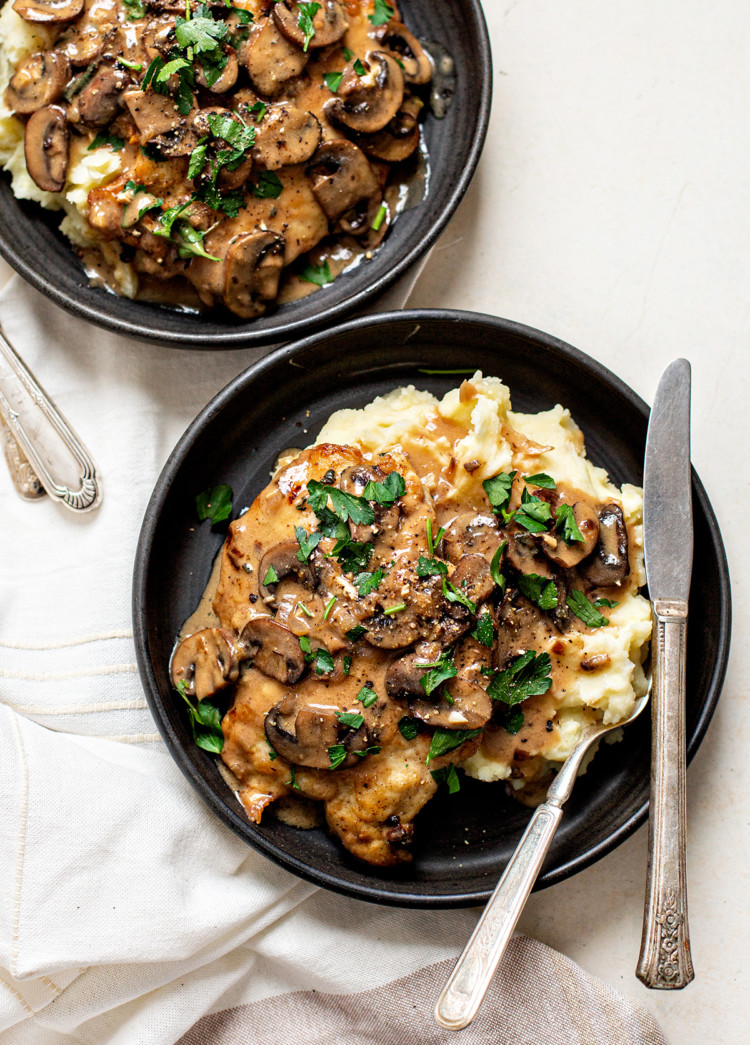 two black dishes plated with chicken marsala and mashed potatoes