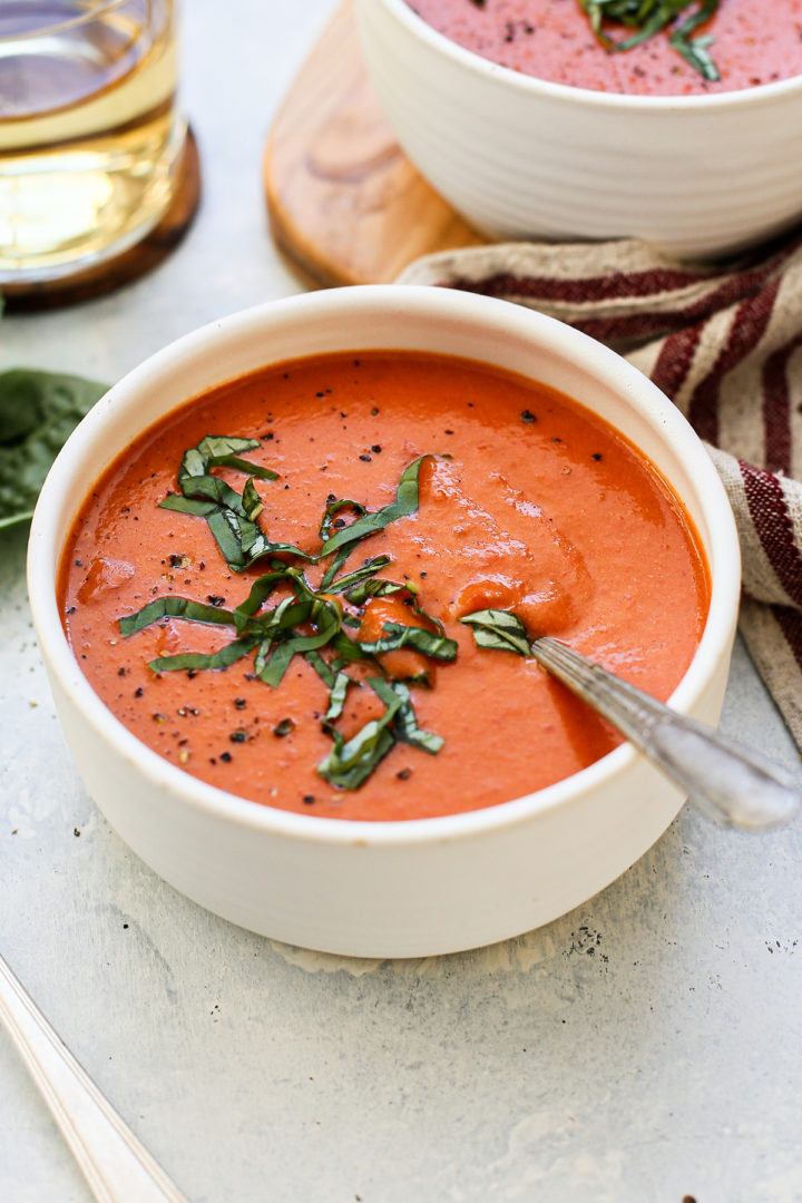 this recipe for cream of tomato soup being served in a white bowl topped with fresh basil