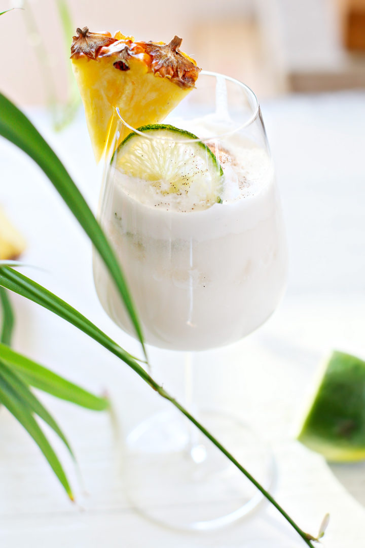 close up photo of a pina colada on the rocks served in a glass with a wedge of pineapple and slice of lime