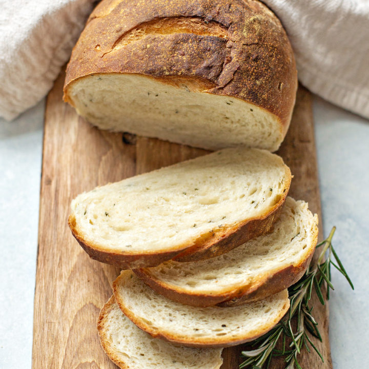 photo of rustic rosemary bread sliced on a cutting board with a sprig of fresh rosemary