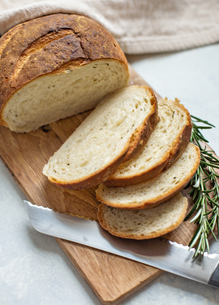 rosemary garlic bread on a wooden cutting board with a bread knife and sprig of fresh rosemary