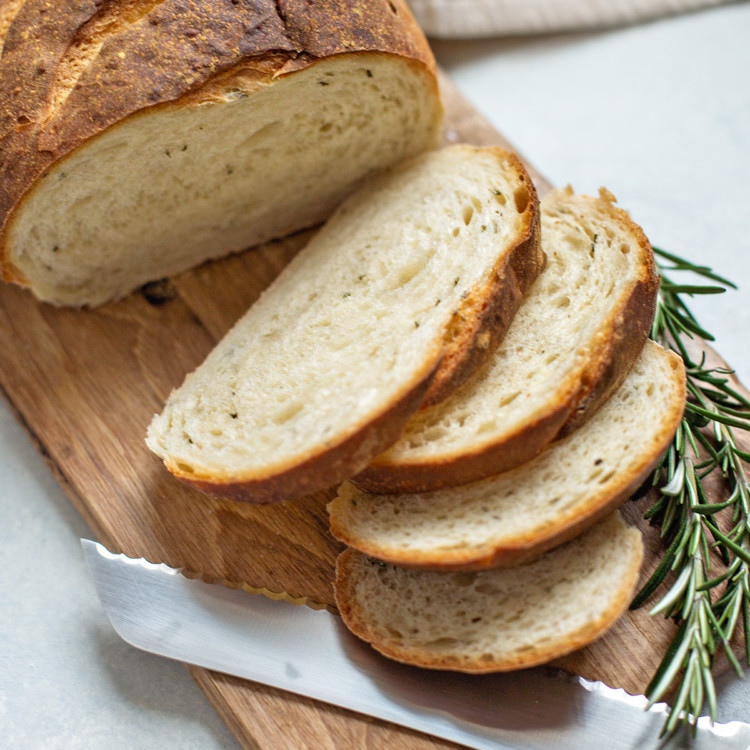 rosemary garlic bread on a wooden cutting board with a bread knife and sprig of fresh rosemary