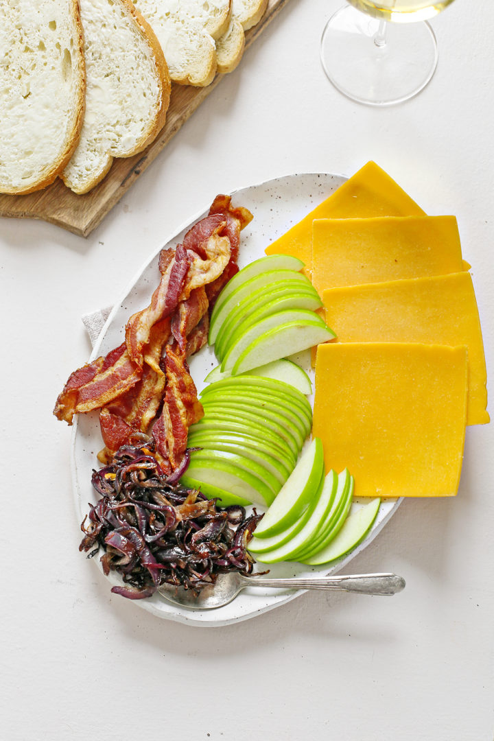 caramelized onions, apples, cheddar cheese, and bacon on a white plate to make a grilled cheese with bacon sandwich
