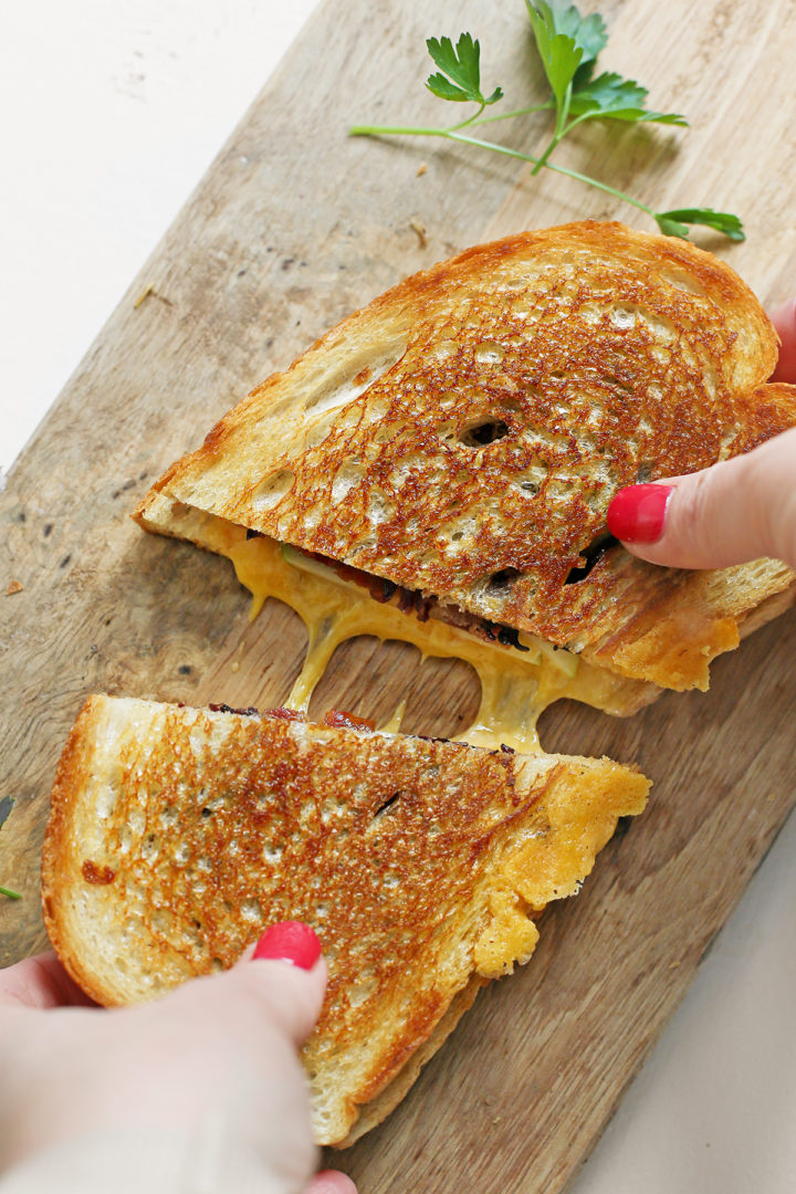 woman pulling apart a bacon and apple grilled cheese sanwich
