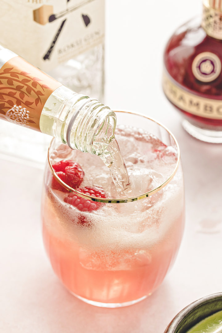 photo of someone preparing a floradora recipe by adding ginger beer to the raspberry gin cocktail in the glass