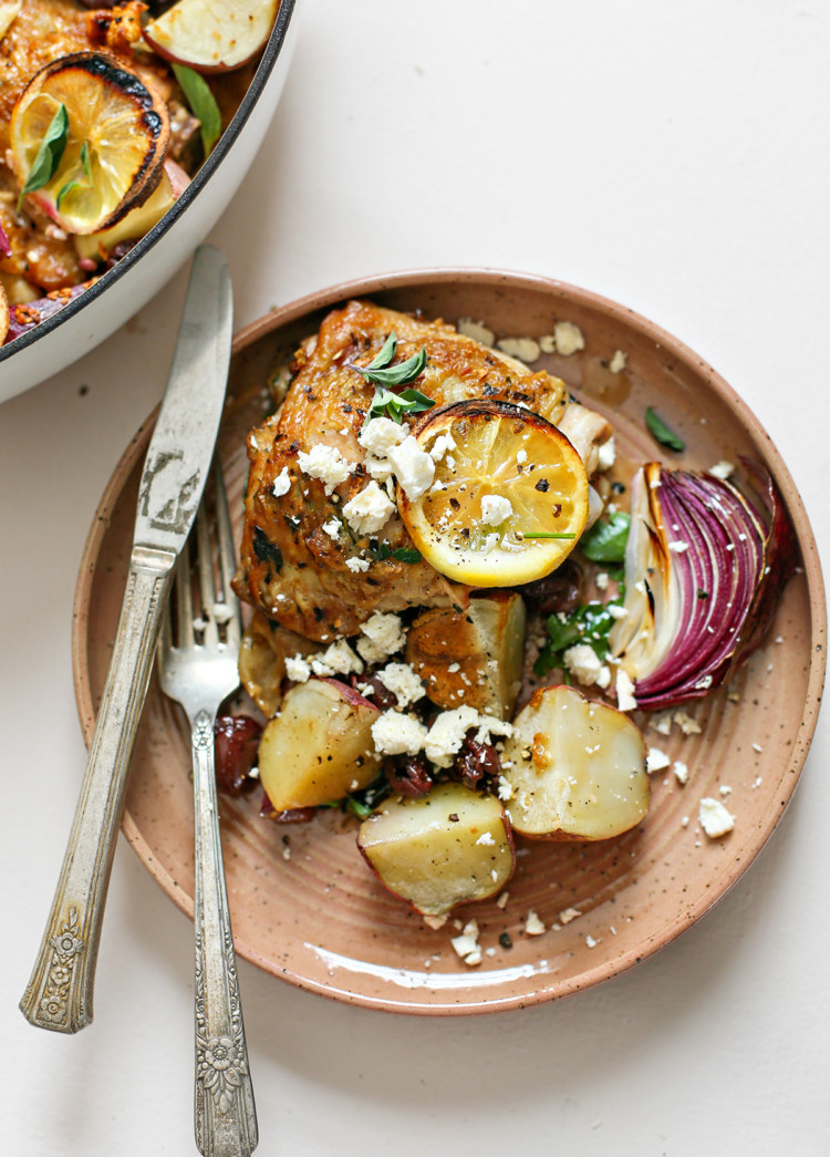 overhead photo of greek chicken thighs on a plate with potatoes, lemons, olives, and feta