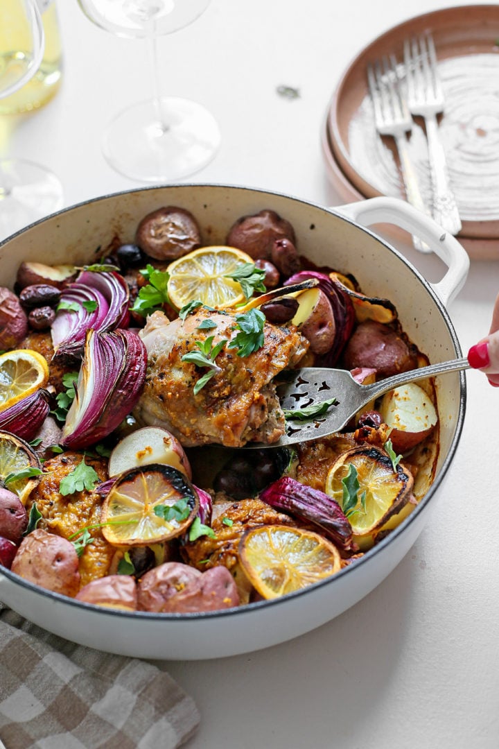 woman serving greek chicken thighs from a cast iron pan