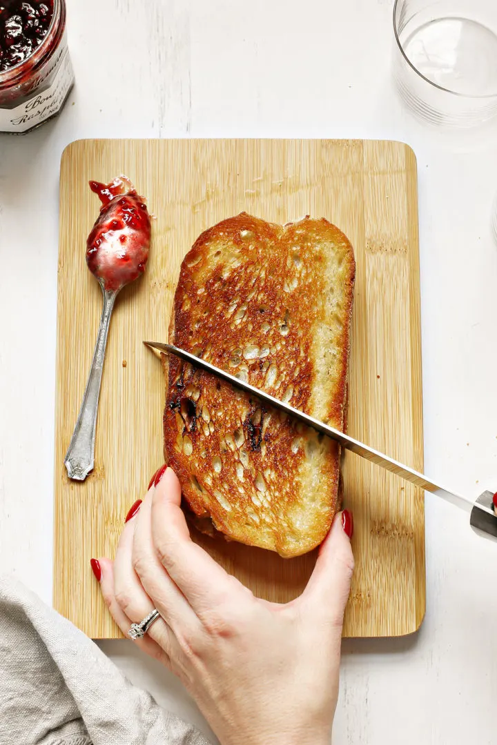 woman slicing a jam, bacon brie sandwich on a wooden cutting board