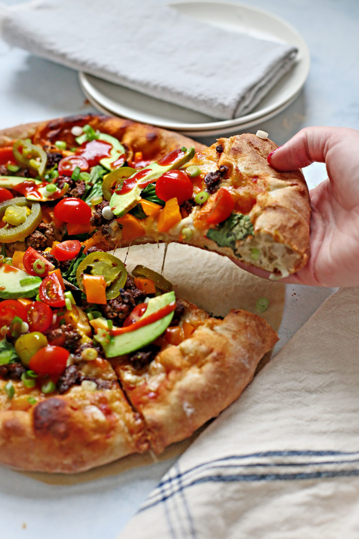 woman picking up a slice of taco pizza