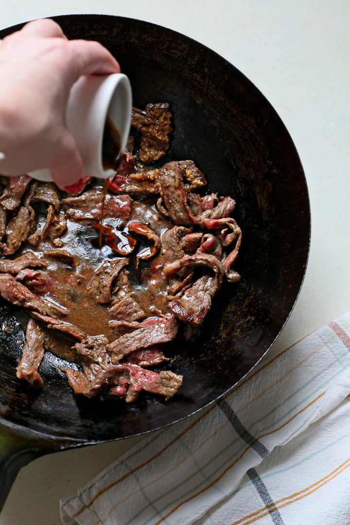 woman adding the beef and broccoli sauce to this flank steak cooking in a wok for  