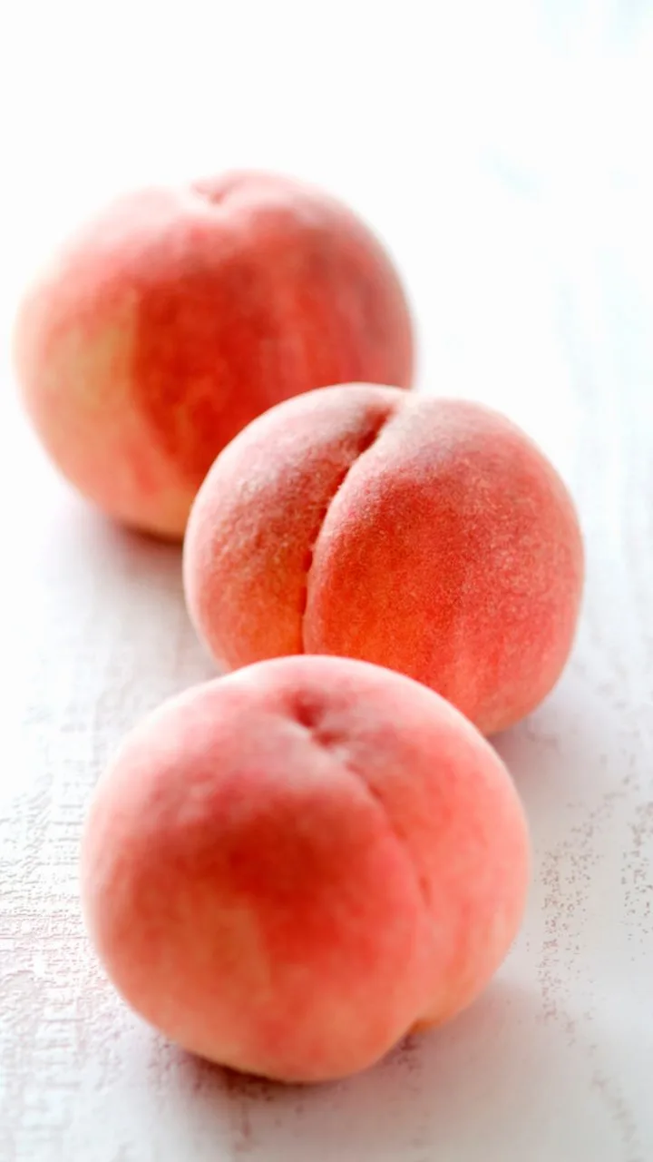 3 peaches on a white wooden table to  prepare for freezing