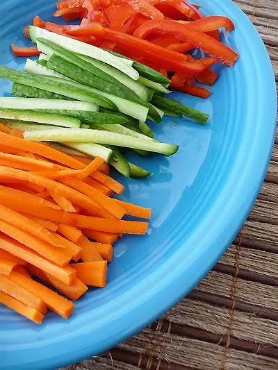 a blue plate with sliced ingredients for spring rolls
